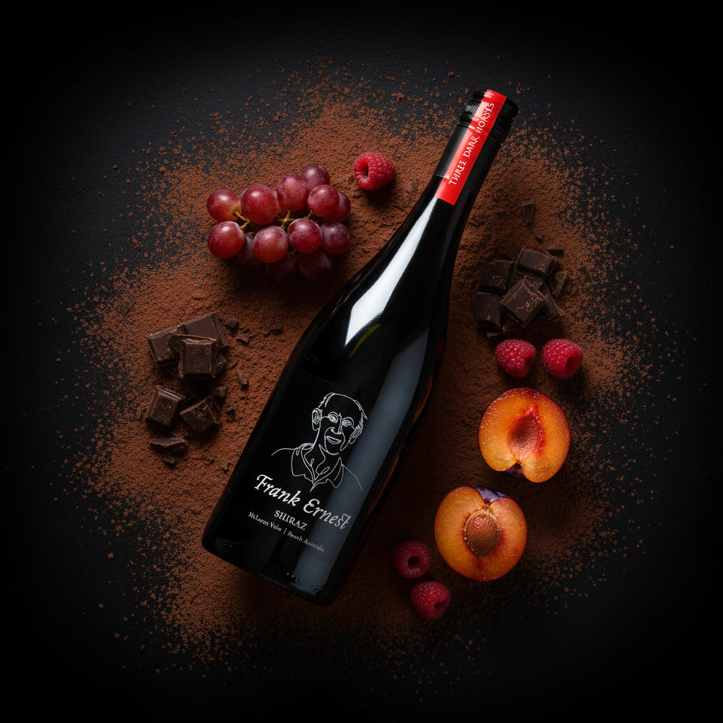 Load image into Gallery viewer, Frank Ernest Shiraz red wine bottle with a label featuring a face, surrounded by fruits and chocolate on a dark surface.