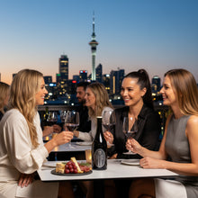 Load image into Gallery viewer, Group of women enjoying a meal with wine glasses and a bottle of Frenchmans Hill Expatrius Syrah against a city skyline.