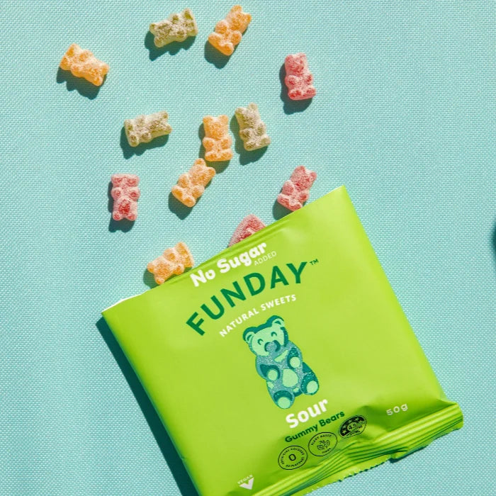 Load image into Gallery viewer, A bright green bag of Funday Sour Vegan Gummy Bears lies on a light aqua background with several loose sour gummy bears scattered above it. The bag shows the Funday brand name and a blue teddy bear logo, with text reading 'No Sugar Added,' 'Natural Sweets,' and 'Sour.