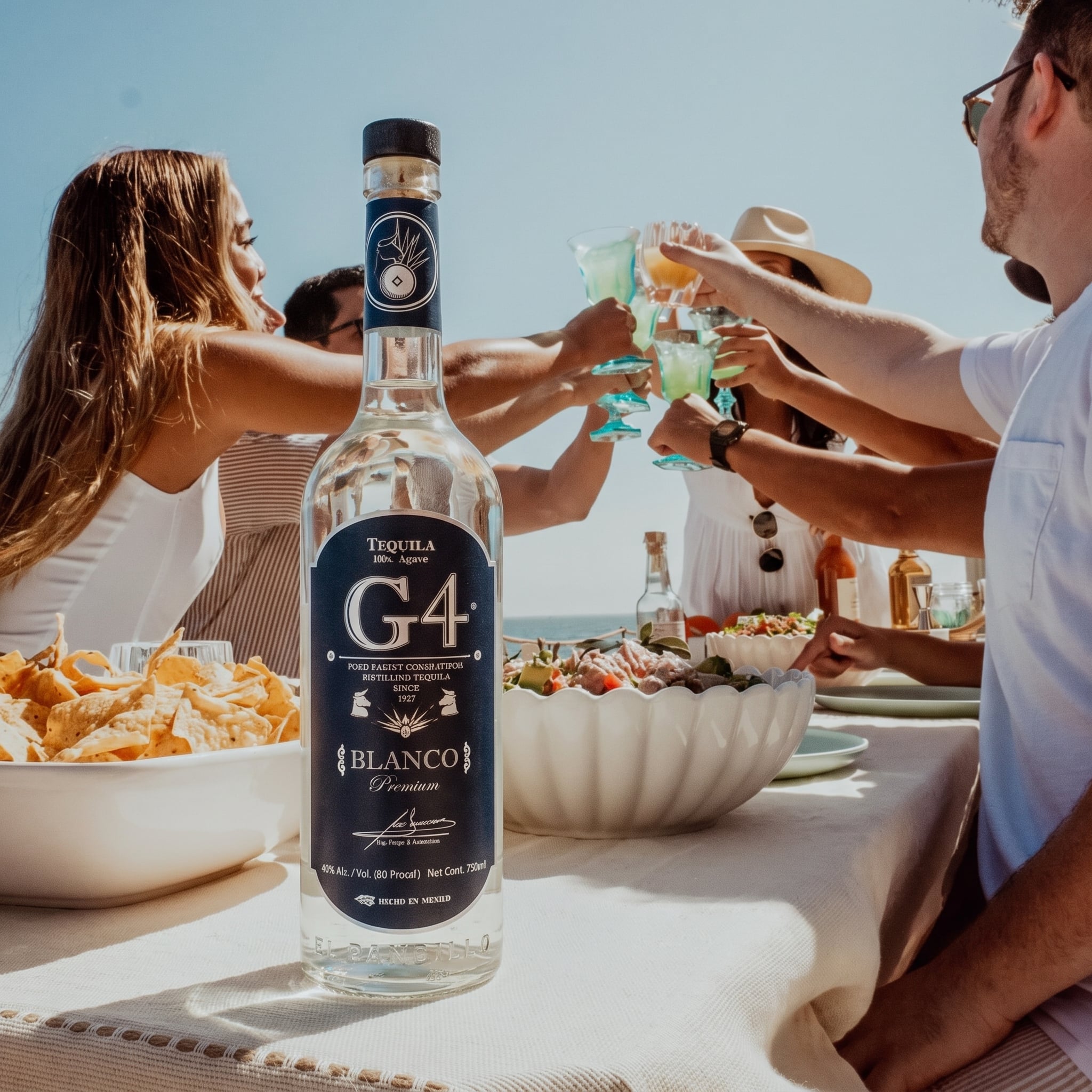 Load image into Gallery viewer, A bottle of G4 Tequila Blanco is prominently displayed on a table outdoors, with people clinking margarita glasses in the background under a bright blue sky.