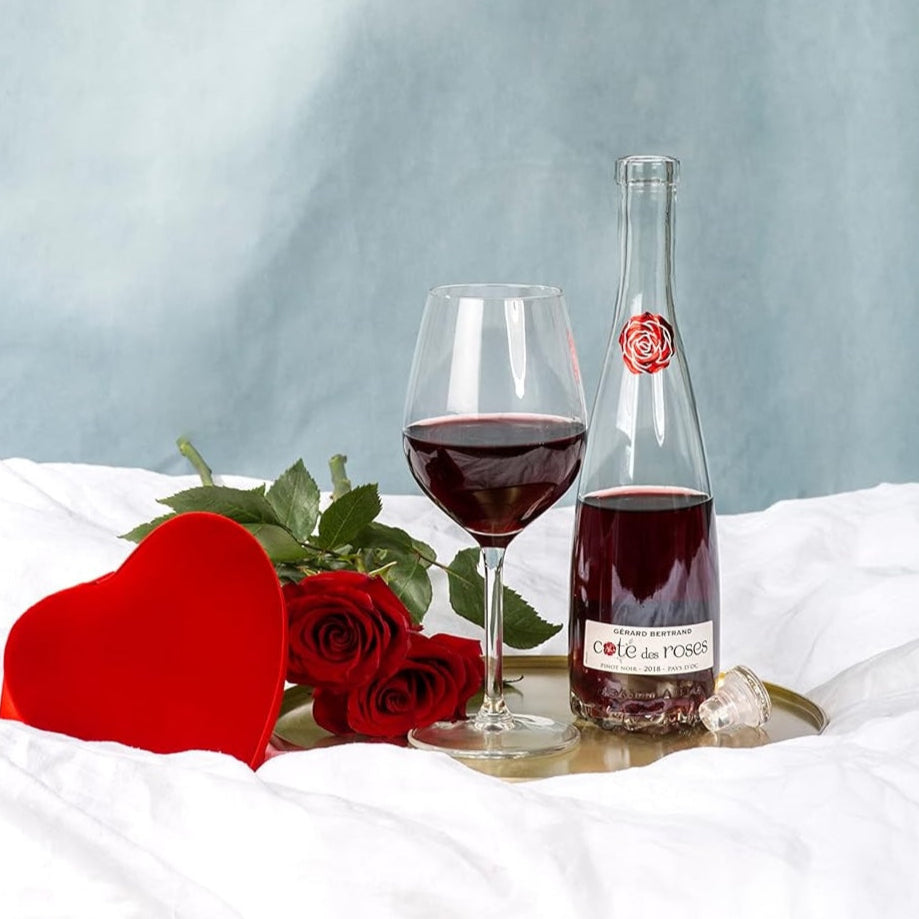 Load image into Gallery viewer, Bottle of GERARD BERTRAND COTE DES ROSE PINOT NOIR ed wine, glass, and roses on a white surface with a light blue background