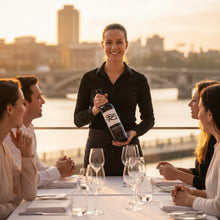 Load image into Gallery viewer, Waitress holding a bottle of Glaetzer-Amon-Ra-Barossa-Shiraz wine for a group of people at an outdoor dining table with a cityscape in the background.