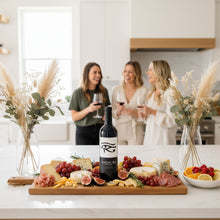 Load image into Gallery viewer, Three women in a kitchen enjoying a bottle of Glaetzer-Amon-Ra-Barossa-Shiraz wine and a charcuterie board with fruits, cheese, and a bottle of Amon Ra wine.