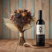 Load image into Gallery viewer, Bouquet of dried flowers next to a bottle of Glaetzer-Barossa-Valley-Bishop-Shiraz wine on a wooden surface.