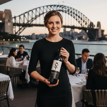 Load image into Gallery viewer, Woman holding a bottle of Glaetzer-Barossa-Valley-Bishop-Shiraz wine with the Sydney Harbour Bridge in the background