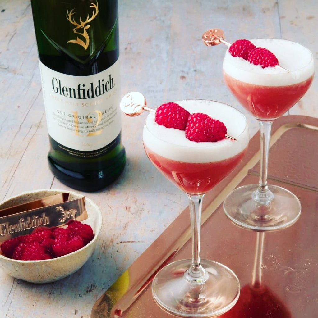 Two cocktail glasses with red and white drinks and raspberries, next to a bottle of Glenfiddich 12 year old single malt whisky.