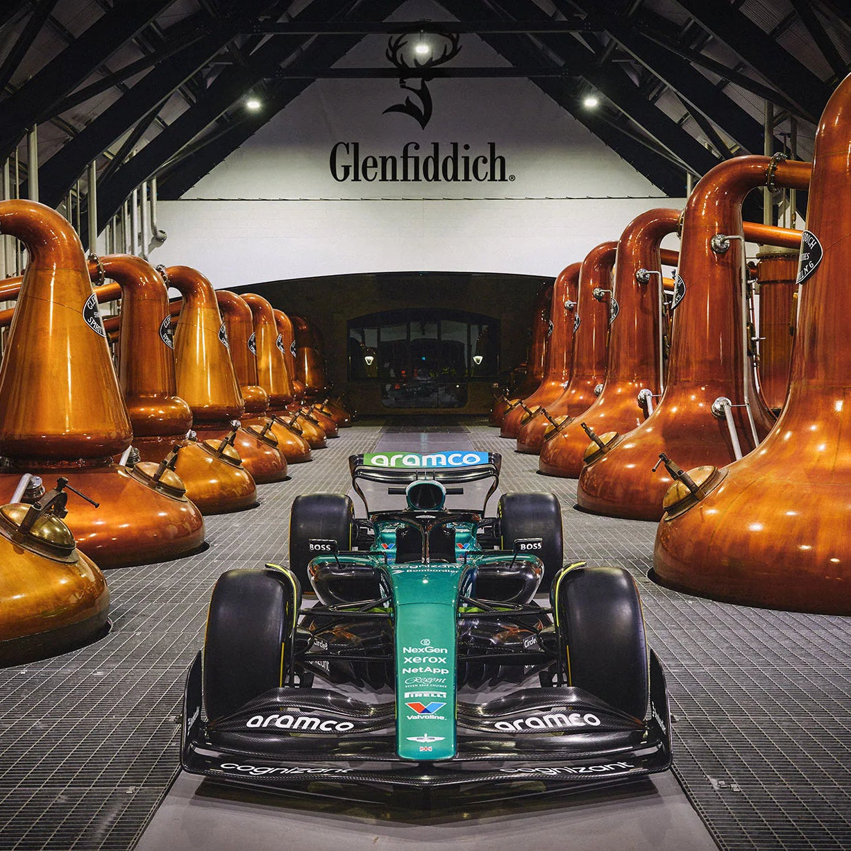 Load image into Gallery viewer, Aston Martin Formula 1 car in the Glenfiddich distillery in between large copper stills.