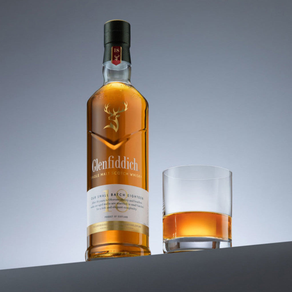Load image into Gallery viewer, Glenfiddich 18 year old single malt whisky bottle with a glass of whisky on a grey background