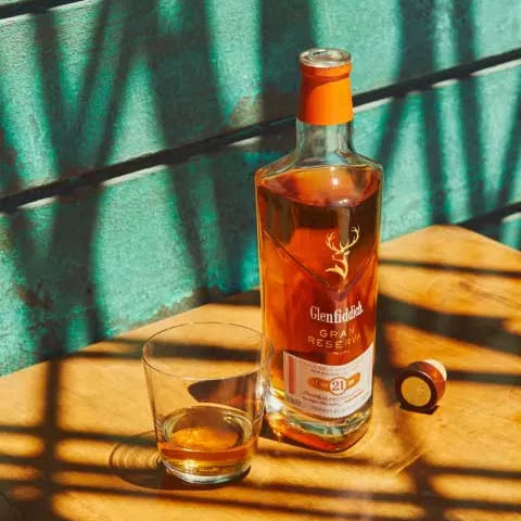 Load image into Gallery viewer, Glenfiddich 21 year old Whisky bottle and glass on a wooden table with green curtain background