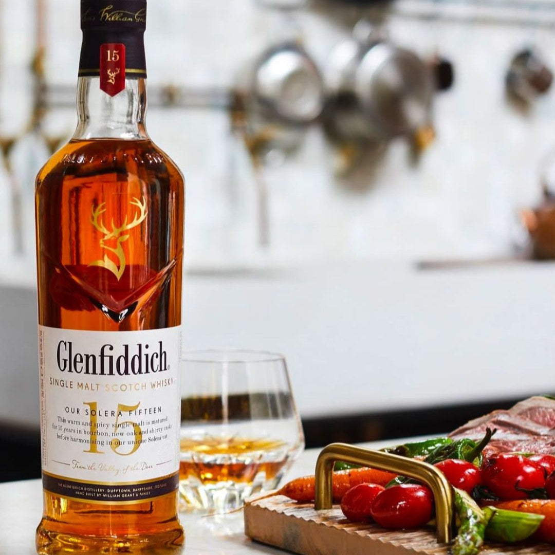 Load image into Gallery viewer, Bottle of Glenfiddich 15 year old whisky with a glass and appetisers on a table.