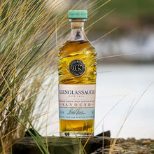 Load image into Gallery viewer, Bottle of Glenglassaugh whiskey on a pebbly beach with grasses.