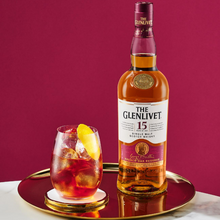 Load image into Gallery viewer, Bottle of The Glenlivet 15 single malt Scotch whisky with a glass of cocktail on a red background