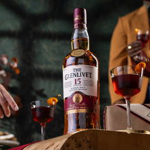 Load image into Gallery viewer, The Glenlivet 15-year-old whisky bottle with two glasses of red wine on a wooden surface.