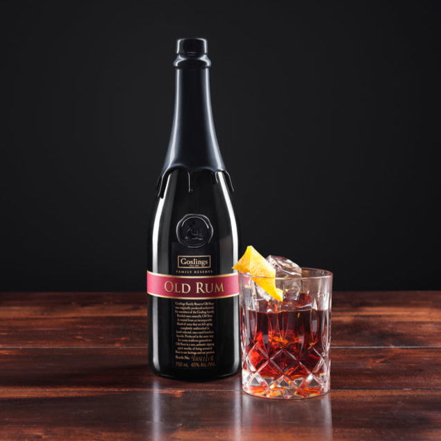 Bottle of Goslings-Old-Family-Bermuda-Reserve-Rum on a wooden surface with a cocktail garnished with a lemon twist.