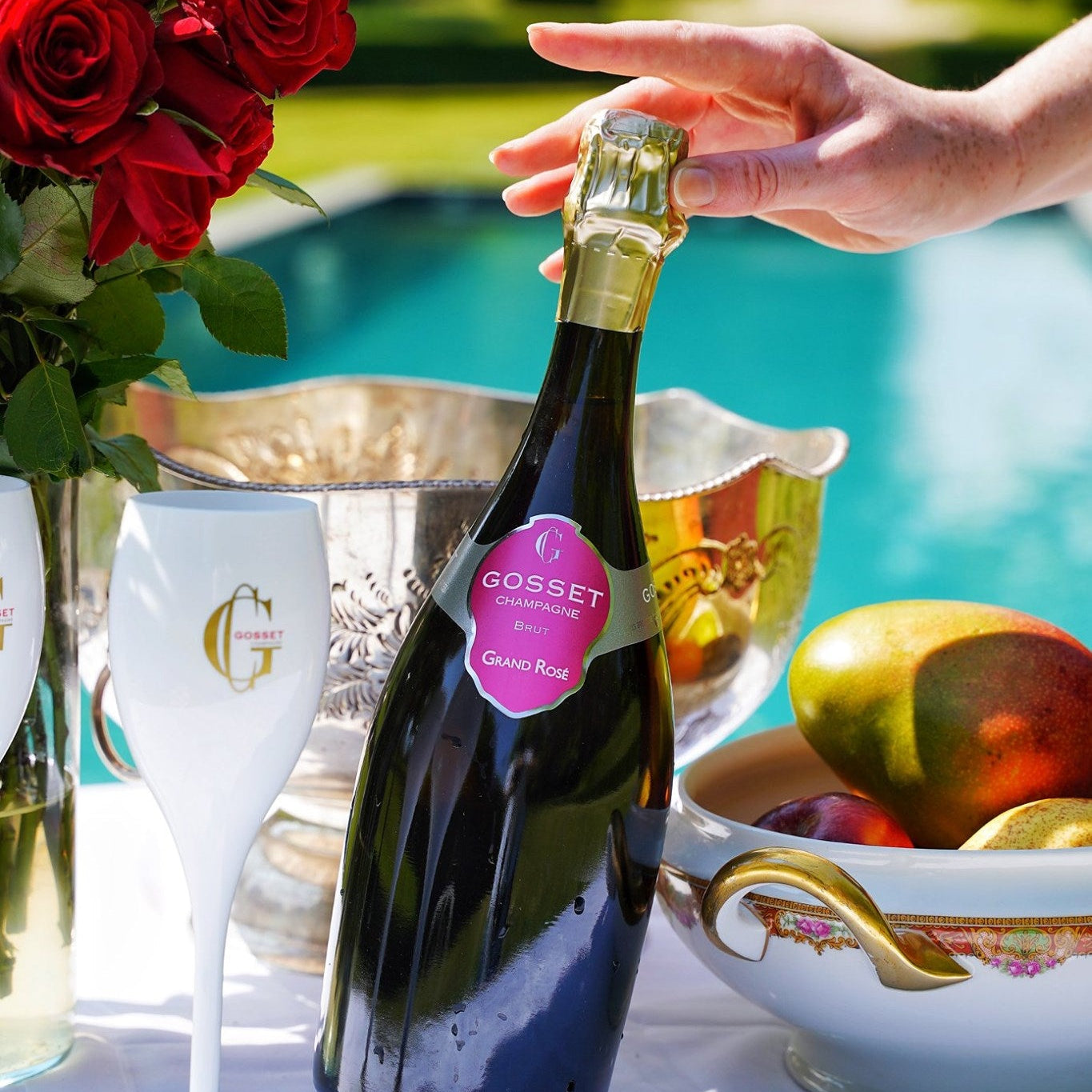 Load image into Gallery viewer, Bottle of Gosset rosé champagne with a hand holding it, surrounded by fruit and glasses outdoors.