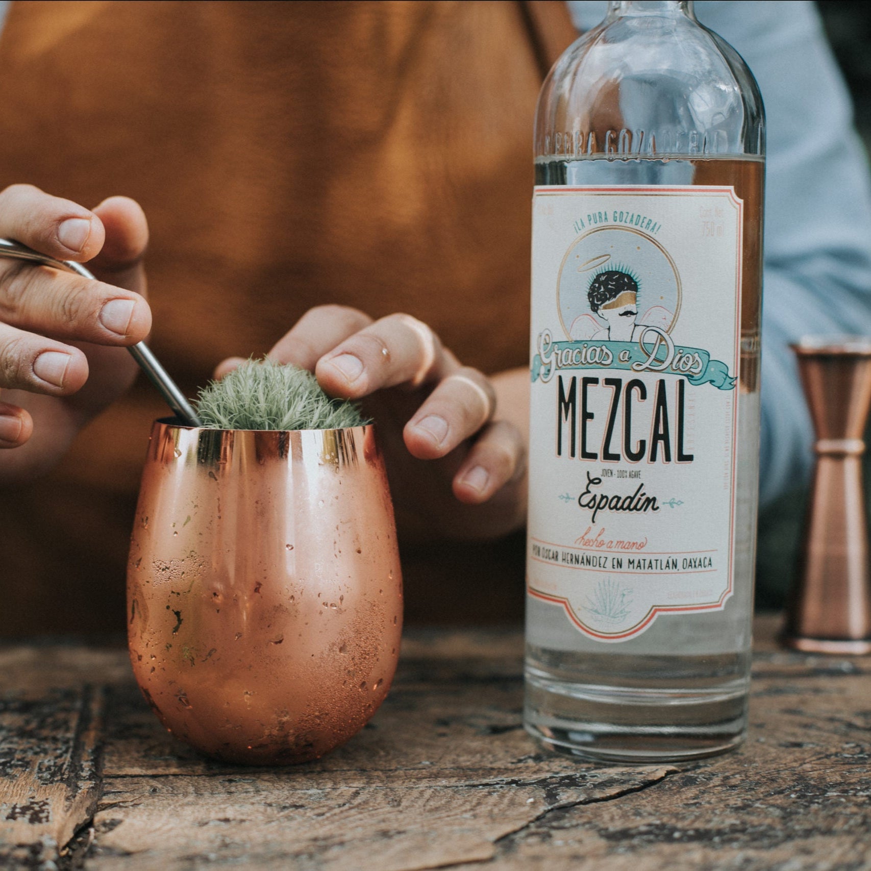 Load image into Gallery viewer, Person preparing a cocktail with a bottle of Mezcal on a rustic surface