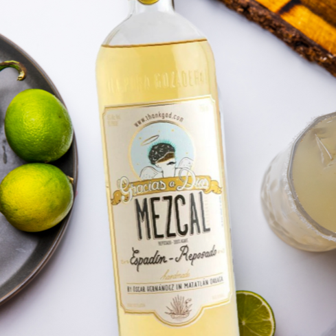 Load image into Gallery viewer, Bottle of mezcals with limes, jalapeño, and a cocktail on a white surface