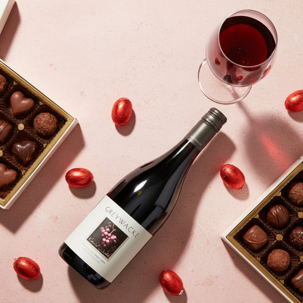 Bottle of Greywacke Pinot Noir wine with a glass and chocolate truffles on a pink surface