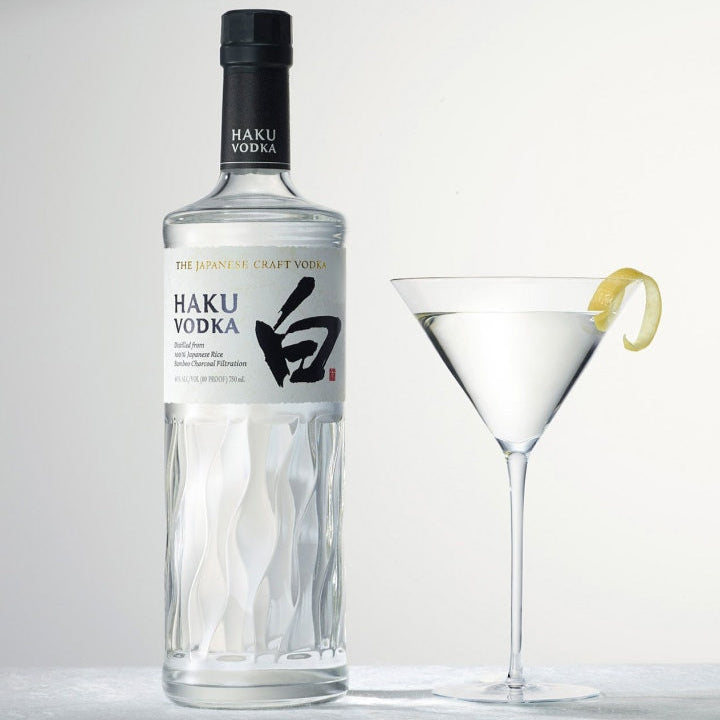 Haku Vodka bottle with a cocktail glass containing a lemon twist on a light gray background