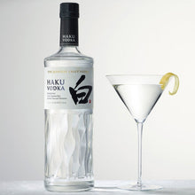 Load image into Gallery viewer, Haku Vodka bottle with a cocktail glass containing a lemon twist on a light gray background