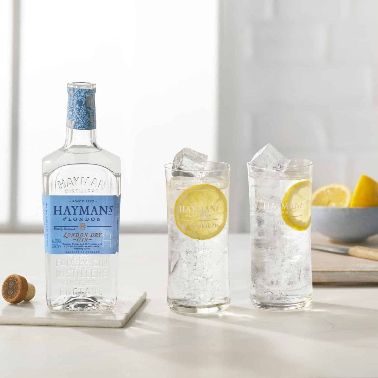Load image into Gallery viewer, Hayman's gin bottle with two glasses of gin and tonic on a table.