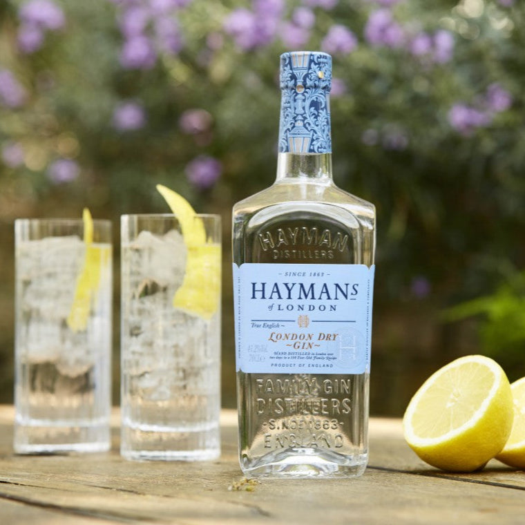Load image into Gallery viewer, Hayman's gin bottle with two glasses and lemons on a wooden table outdoors.