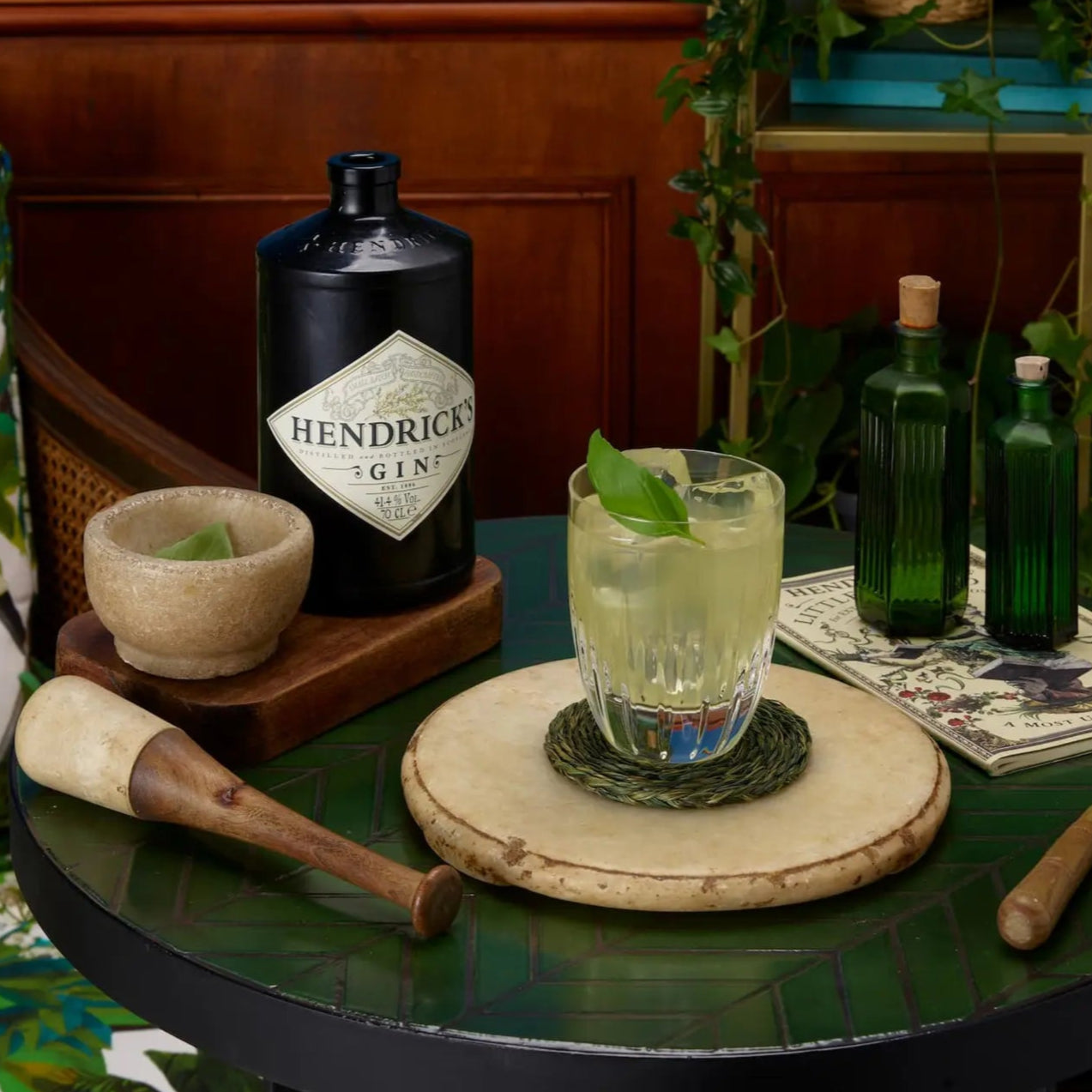 Load image into Gallery viewer, Hendrick's gin bottle on a table with a cocktail and garnishes in a decorative setting.