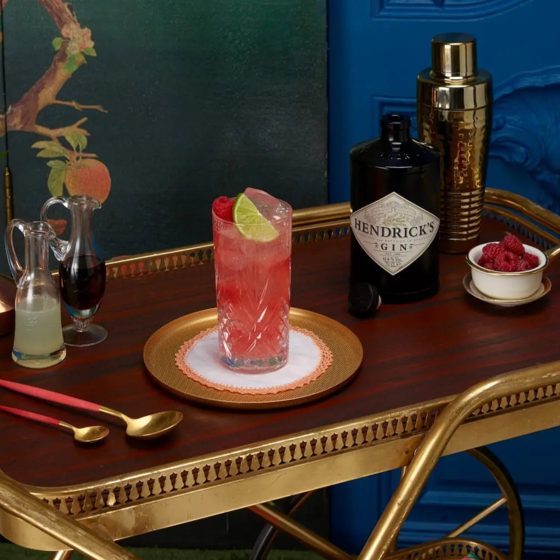 Load image into Gallery viewer, Bar tray with a cocktail, Hendrick's gin bottle, and garnishes against a decorative wall.