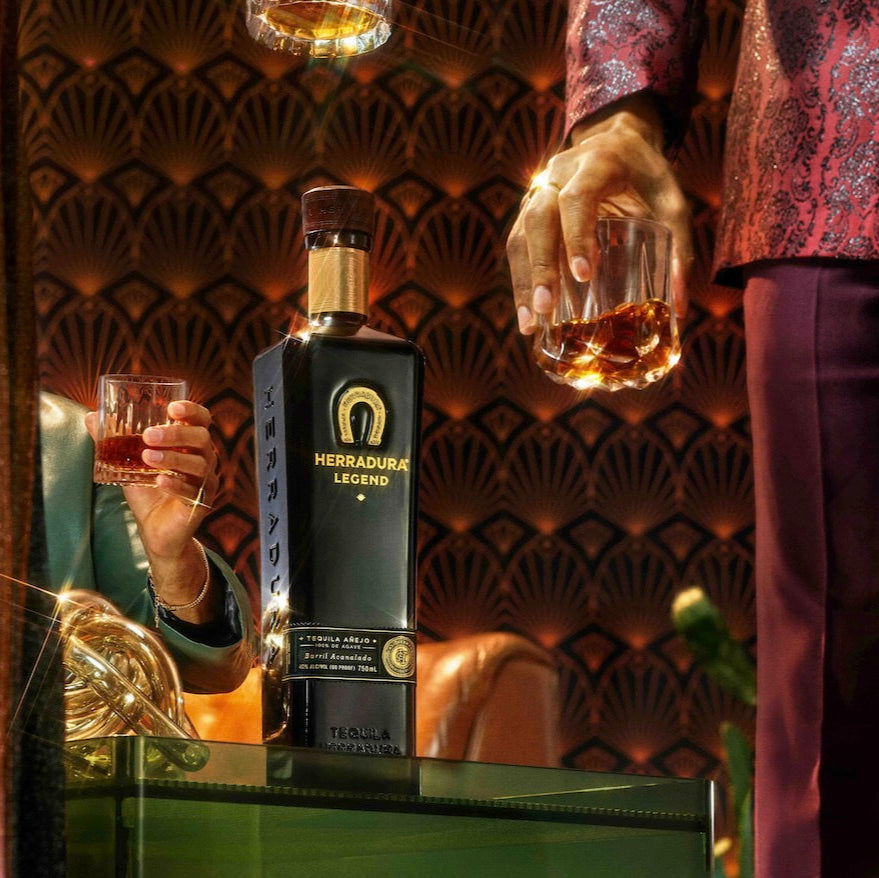 Load image into Gallery viewer, Person holding a bottle of Herradura Anejo Legend Tequila and a glass in a luxurious setting.