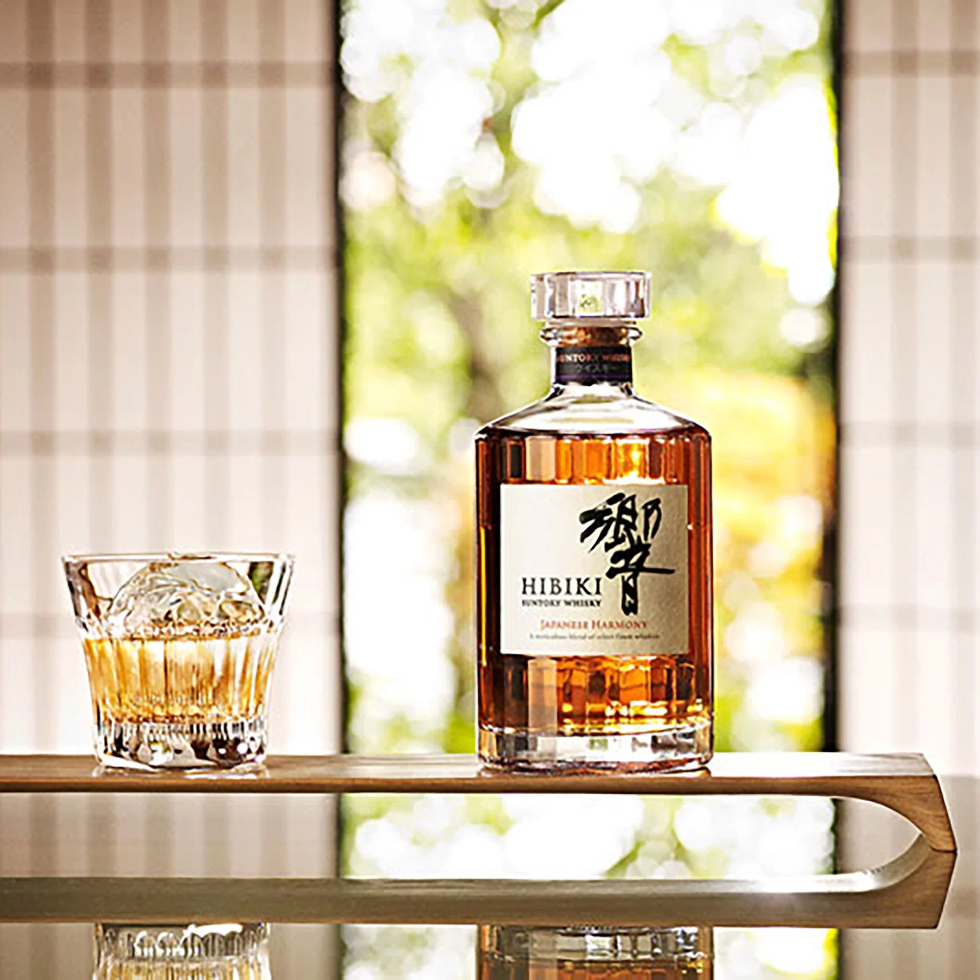 Load image into Gallery viewer, A bottle of japanese Habiki Whisky with a tumbler of neat whisky on a table with a blurred background of a garden