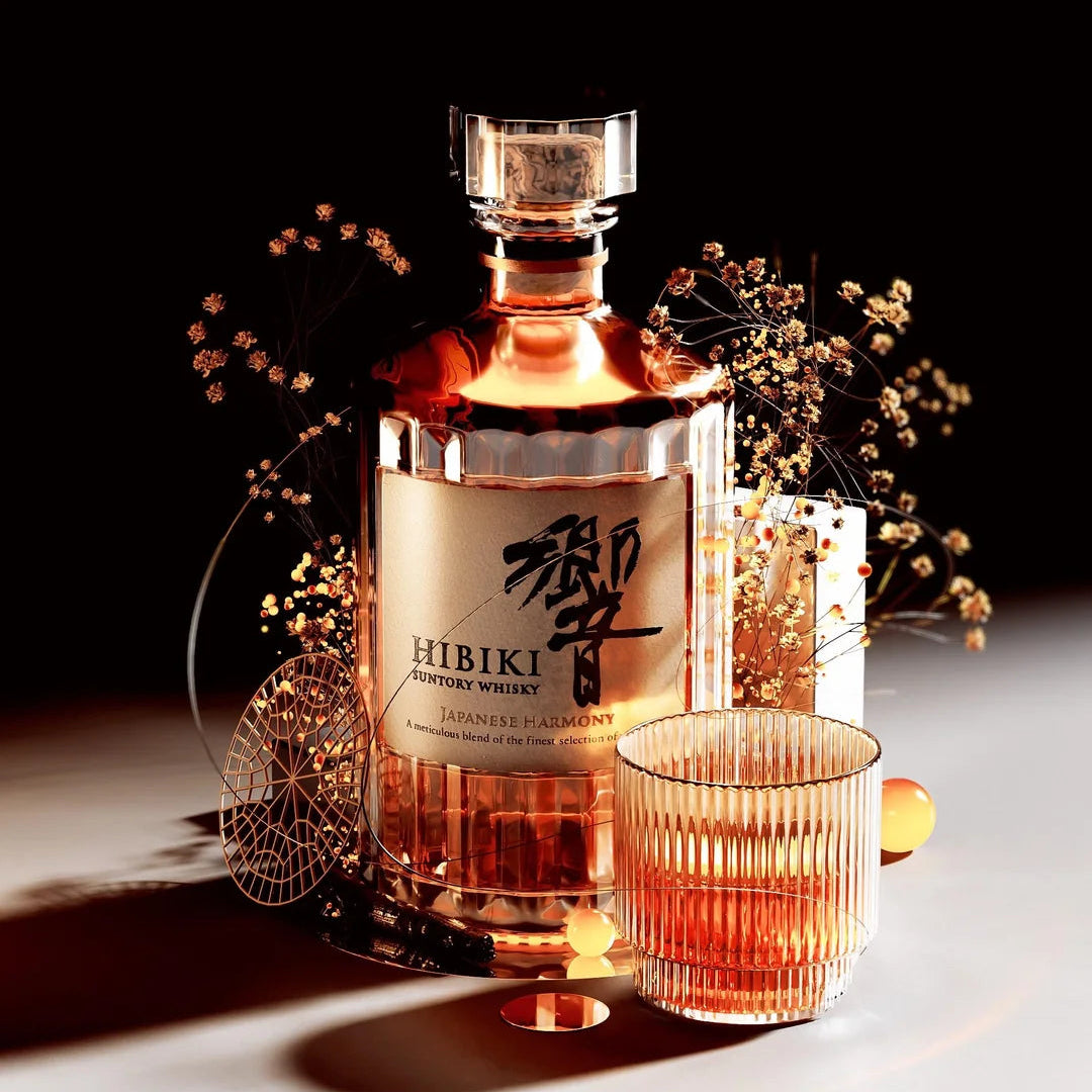 Load image into Gallery viewer, A clear glass bottle of Hibiki Harmony Japanese Whisky, a matching ribbed glass tumbler, and decorative dried florals against a black background.