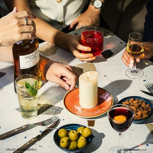 Load image into Gallery viewer, People enjoying drinks at a table with a bottle of Highland Park 12 year old whisky, candle and snacks