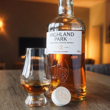 Load image into Gallery viewer, Highland Park 12 year old whisky bottle with a glass on a wooden table