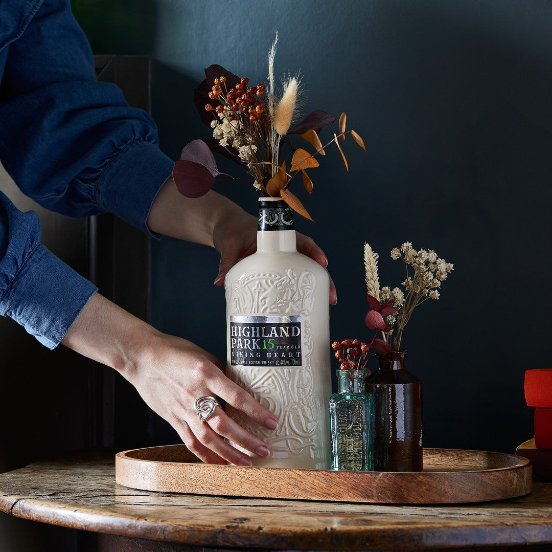 Load image into Gallery viewer, Person holding a Highland Park whisky bottle on a wooden tray with decorative elements.