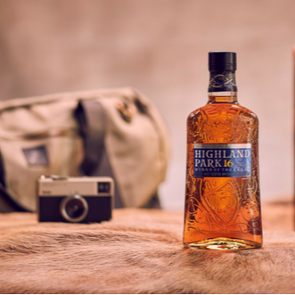 Bottle of Highland Park whisky on a wooden surface with a camera and bag in the background