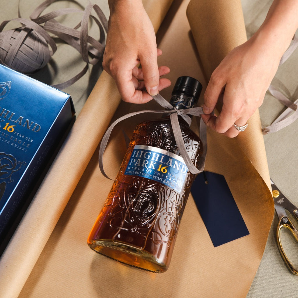 Person wrapping a bottle of Highland Park 16 whisky with brown paper and a ribbon.