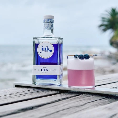 Load image into Gallery viewer, A bottle of gin and a cocktail on a beach.