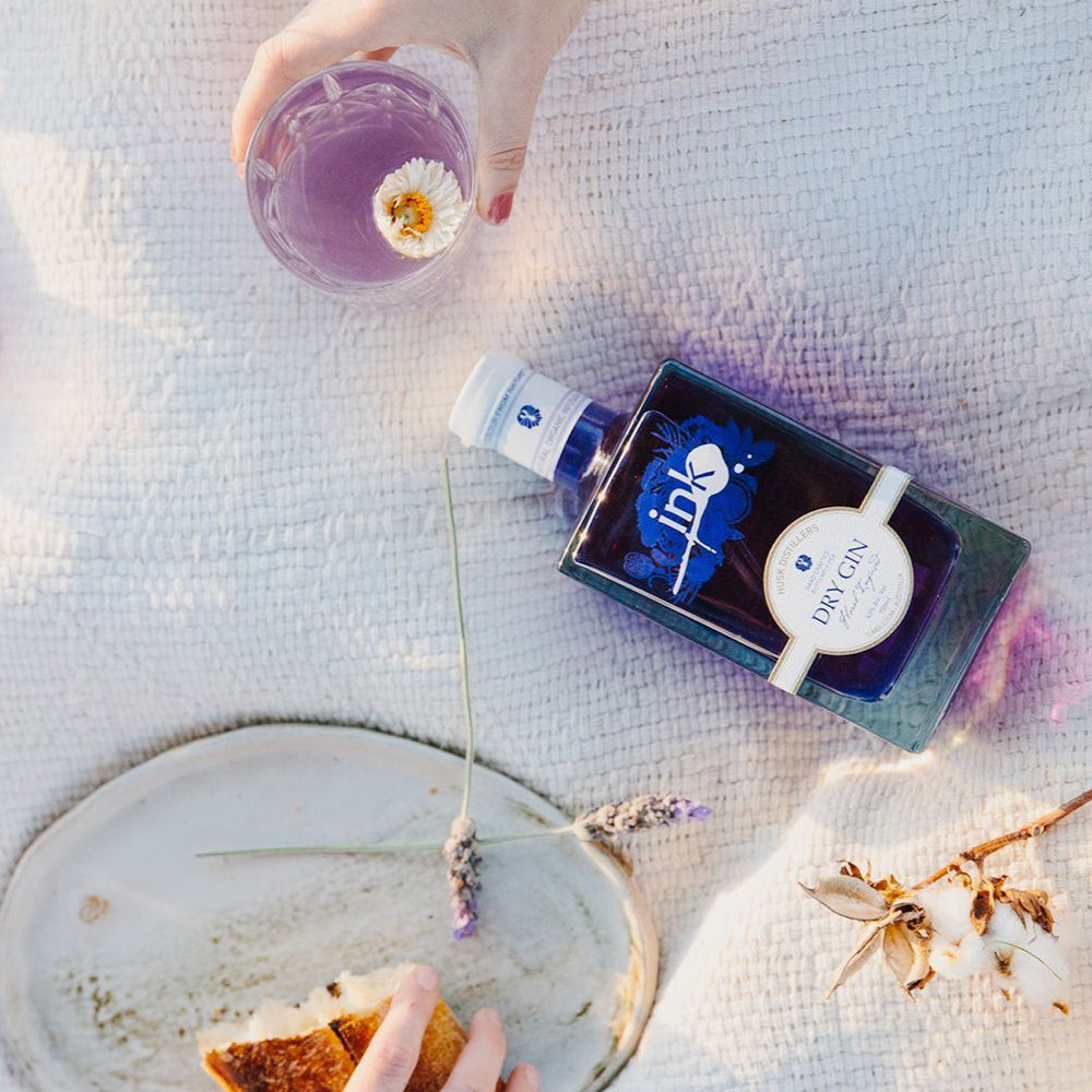 Load image into Gallery viewer, Person enjoying an INK gin &amp; tonic with lavender twigs on a textured surface.