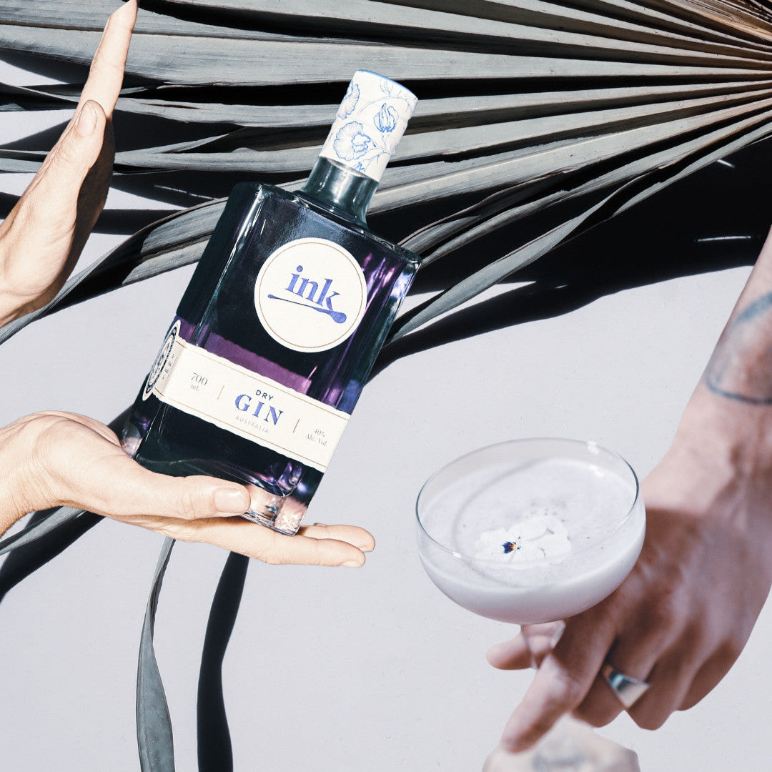 Load image into Gallery viewer, Bottle of 'ink' gin held by a hand with a palm leaf in the background