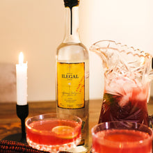 Load image into Gallery viewer, Bottle of Ilegal Joven Mezcal with cocktails and a candle on a wooden surface