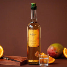 Load image into Gallery viewer, Bottle of Ilegal Reposado Mezcal with a glass of orange juice and fruits on a wooden board against a brown background
