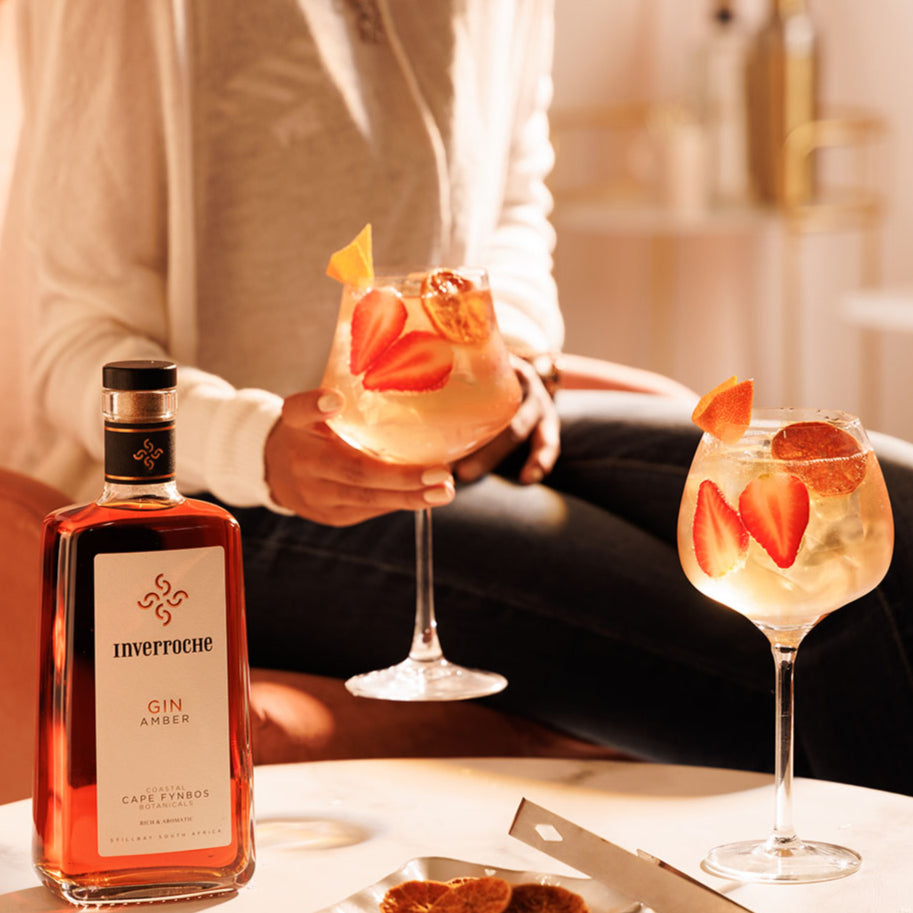 Load image into Gallery viewer, Two glasses of a cocktail with strawberry slices and a bottle of Inverrho Gin Amber on a table.