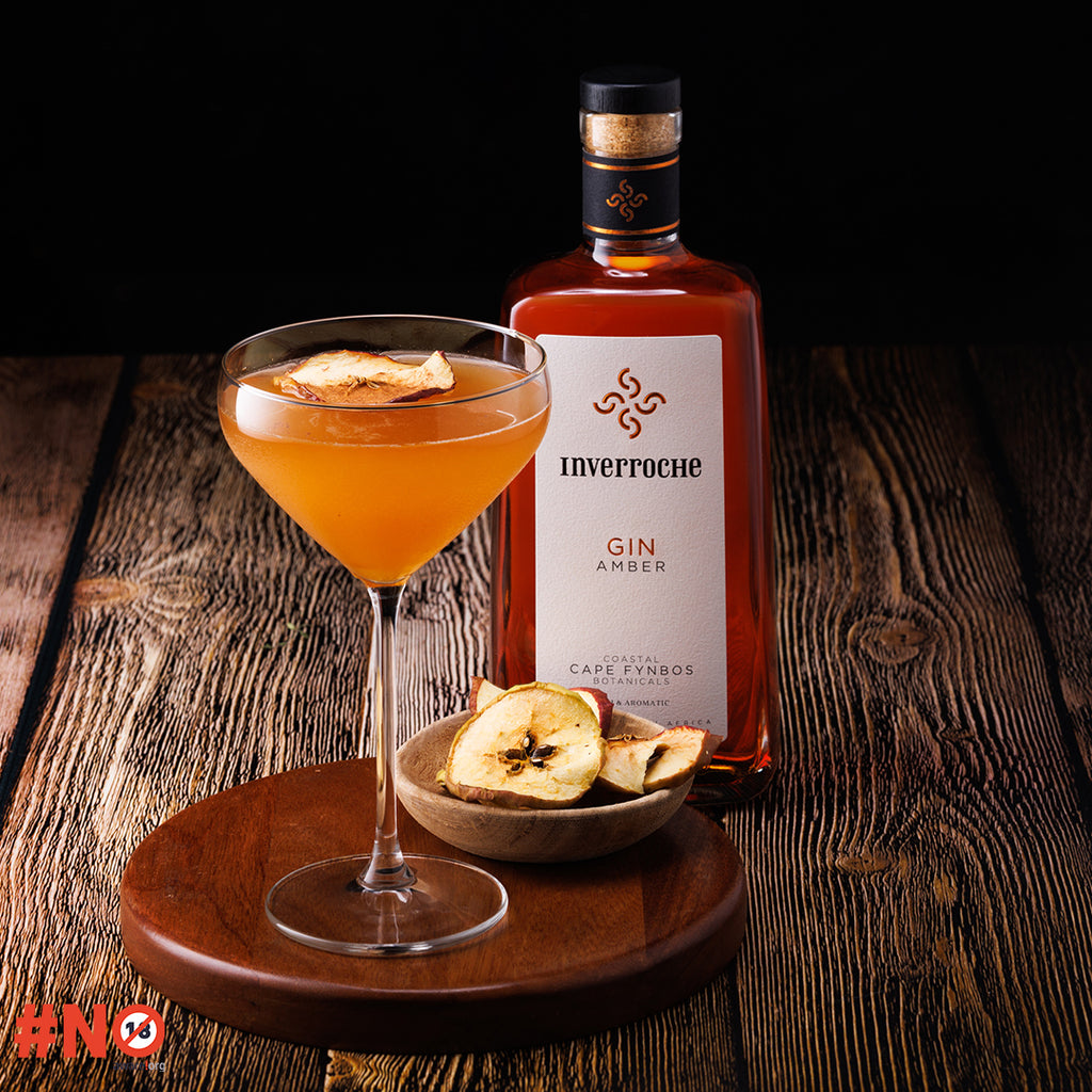 Bottle of Inverroche Gin Amber with a cocktail and dried apples on a wooden surface