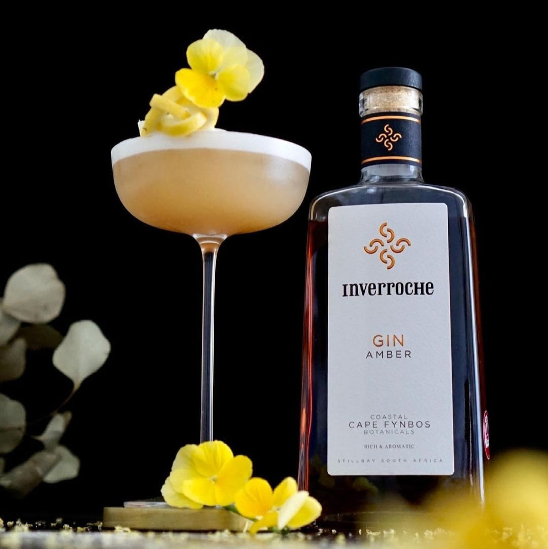 Load image into Gallery viewer, Bottle of Inverroche Gin Amber with a cocktail garnished with flowers on a dark background