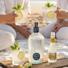 Load image into Gallery viewer, Two people holding Island Navy gin cocktails with lime slices on a beach, featuring Island Gin and Fever-Tree tonic water.