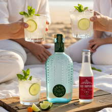 Load image into Gallery viewer, Two people holding glasses of gin and tonic with lime slices, accompanied by a bottle of Island Gin and East Imperial tonic water on a wooden surface.