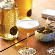 Load image into Gallery viewer, Cocktail in a glass with bottles and olives on a wooden table