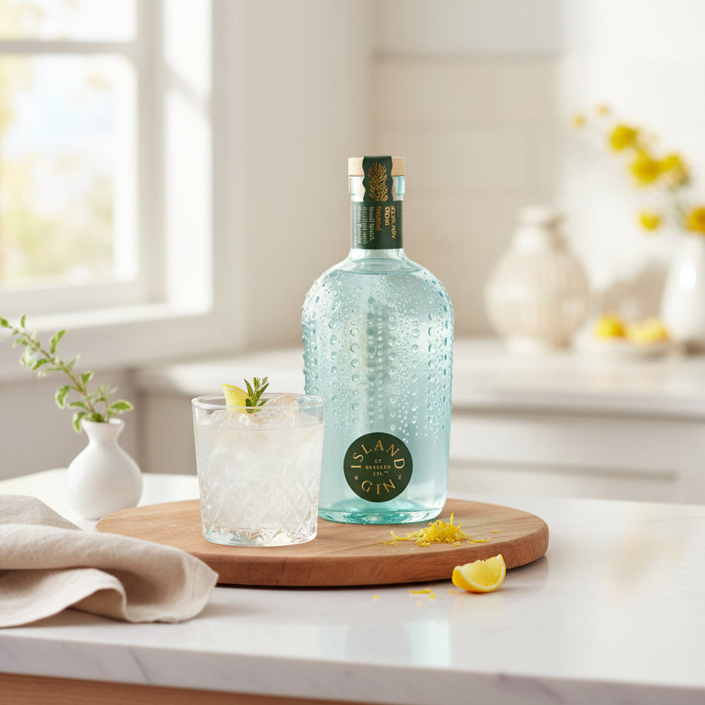 Load image into Gallery viewer, A bottle of Island Original Gin with a textured light blue body and a green circular label, displayed on a wooden board next to a glass of gin with ice and a lemon slice in a bright kitchen setting.