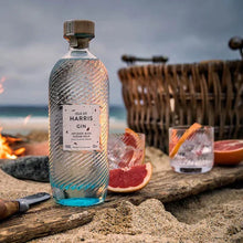 Load image into Gallery viewer, A bottle of gin and glasses on a beach with a lit fire pit in the background.