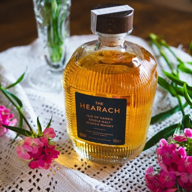 Load image into Gallery viewer, Isle of Harris 'The Hearach' Single Malt Whisky bottle on a table with some decorative flowers beside the bottle